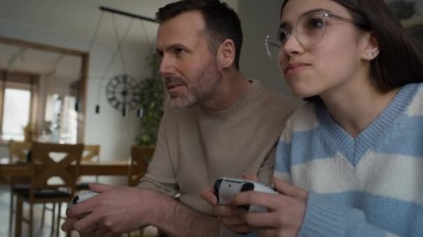 白人のティーンエイジャーの少女と彼女の父親はゲームコントローラーでビデオゲームで遊んでいます 8Kでレッドヘリウムカメラで撮影 — ストック動画