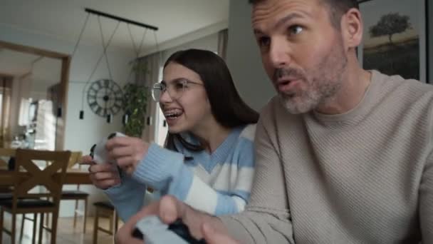 白人のティーンエイジャーの少女と彼女の父親はゲームコントローラーでビデオゲームで遊んでいます 8Kでレッドヘリウムカメラで撮影 — ストック動画