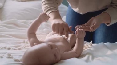 Anne, bebeğin vücuduna nemlendirici merhem sürüyor. 8K 'da kırmızı helyum kamerayla çekildi..     