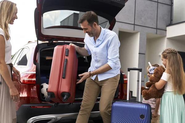 stock image Caucasian family of four packing luggage into car trunk before holiday