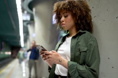 Genç afro kadın cep telefonunu karıştırıyor ve yeraltı dünyasını bekliyor. 