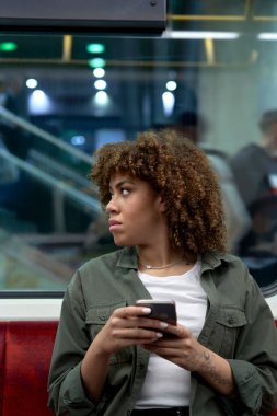 Yeraltında cep telefonunu karıştıran ve gözlerini kaçıran genç afro kadın.