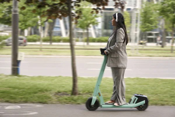 中国のビジネス女性プッシュスクーターに乗って音楽を聴く — ストック写真
