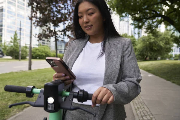 ビジネス中国人女性持っていますビデオ通話ながらプッシュスクーターに乗って — ストック写真