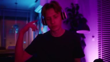 Evde neon ışıkların arasında dans eden genç beyaz bir adam. 8K 'da kırmızı helyum kamerayla çekildi.. 