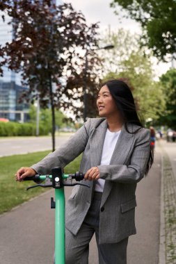 İş kıyafetiyle elektrikli scooter kullanan Çinli bir kadın.