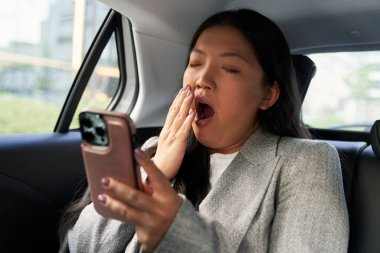 Çinli iş kadını takside cep telefonu kullanıyor ve esniyor.