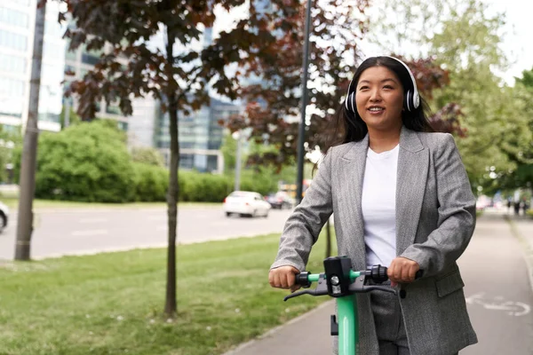 プッシュスクーターに乗って ヘッドフォンで音楽を聴く中国のビジネス女性 — ストック写真