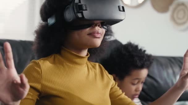 リビングルームでビデオゲームをプレイするために仮想現実シミュレータを身に着けている10代の少女 8Kでレッドヘリウムカメラで撮影 — ストック動画