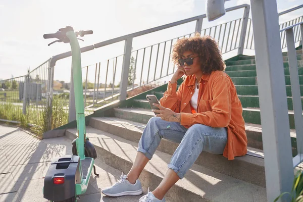 外の階段に座って携帯電話を閲覧している黒人女性 — ストック写真
