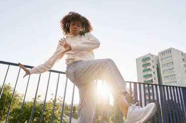 Siyah kadının kulaklık taktığı ve köprüde dans ettiği düşük açı.