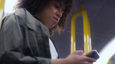 Yeraltında gezen ve cep telefonuna göz atan Afrikalı genç bir kadının düşük açılı görüntüsü. 8K 'da kırmızı helyum kamerayla çekildi.. 