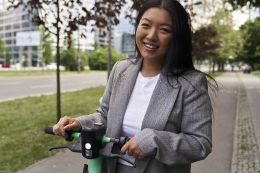 İş kıyafetiyle elektrikli scooterın üzerinde duran Çinli kadının portresi. 