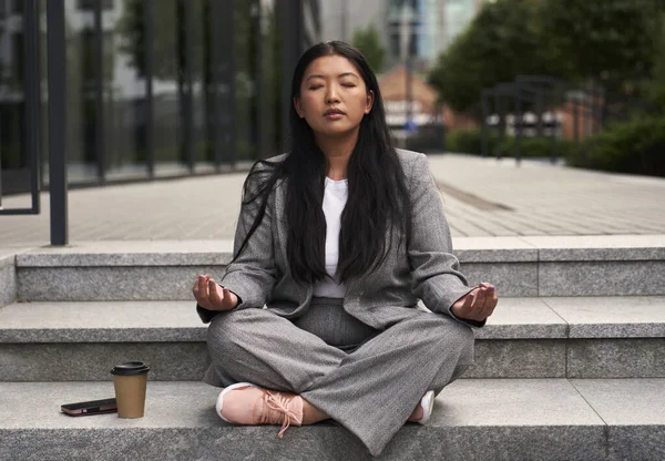 Chinese woman in business outfit meditating out of the building