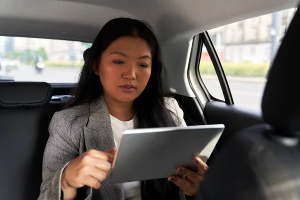 Business Chinese woman driving in a taxi and browsing digital tablet
