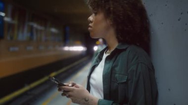 Genç afro kadın platformda duruyor ve yeraltını bekliyor. 8K 'da kırmızı helyum kamerayla çekildi..  