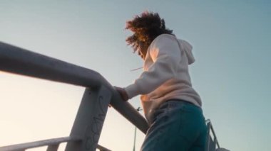 Köprüde dans eden ve kameraya bakan siyah kadının alçak açılı görüntüsü. 8K 'da kırmızı helyum kamerayla çekildi.. 