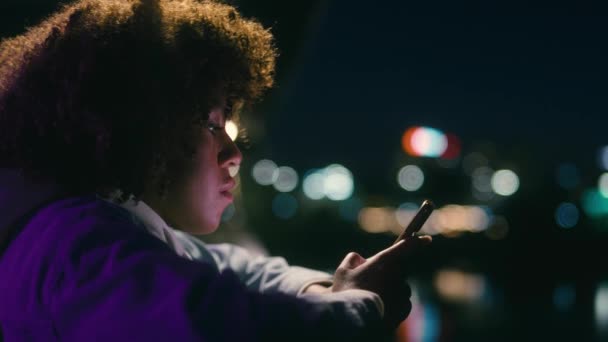 Czarna Kobieta Stojąca Nocą Moście Przeglądająca Swój Telefon Komórkowy Nakręcony — Wideo stockowe