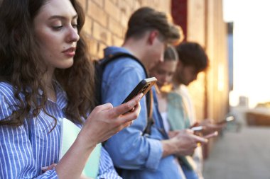 Üniversite öğrencileri üniversite kampüs binasının yanındaki telefonlara bakıyorlar.