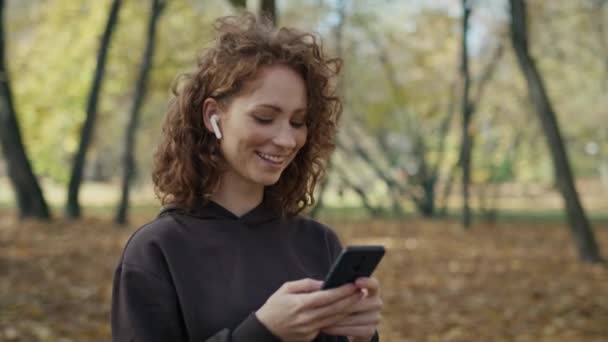 Mujer Pelirroja Sonriente Caminando Por Parque Enviando Mensajes Texto Fotografía — Vídeos de Stock