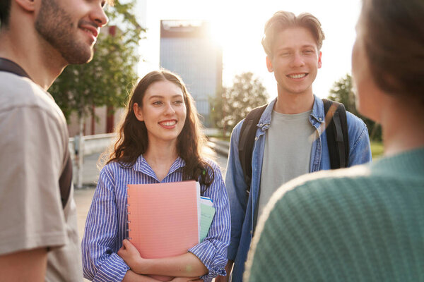 Группа кавказских студентов, стоящих в университетском городке и беседующих