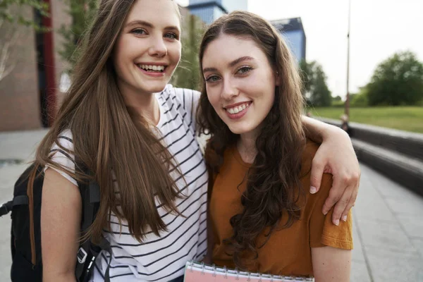 Portrait of two female caucasian university students sitting outside the university campus
