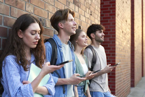 Studenci Uniwersytetu Przeglądający Telefony Obok Budynku Kampusu Uniwersyteckiego — Zdjęcie stockowe