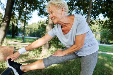 Yaşlı kadın parkta bankta geriniyor.