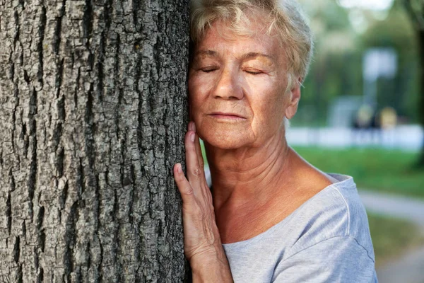 公園の木の横で呼吸運動をしている穏やかなシニア女性 — ストック写真