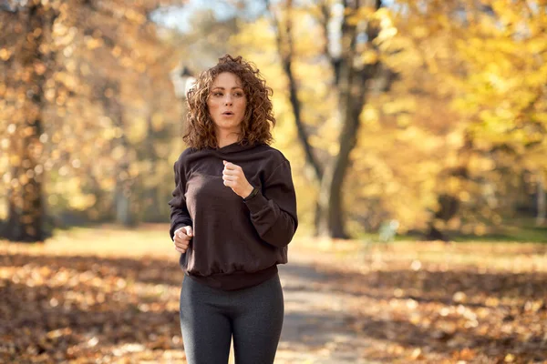 秋天阳光充足的时候 白人妇女在公园里慢跑 — 图库照片