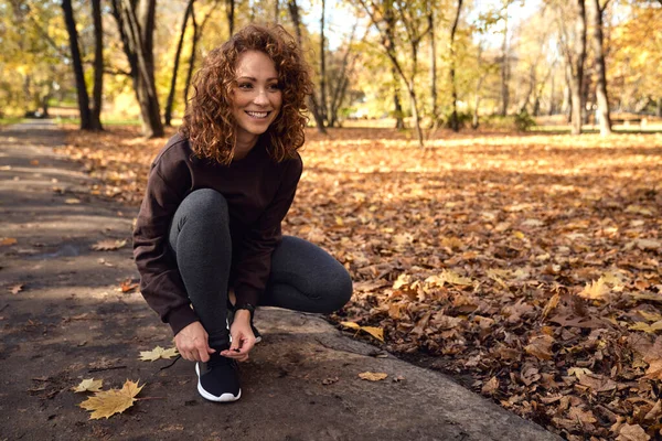 Woman in sports clothes tying shoes with fun before jogging in the park