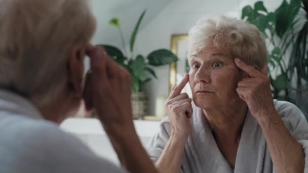 Старшая Женщина Проверяет Состояние Кожи Зеркале Ванной Съемка Красной Гелиевой — стоковое видео