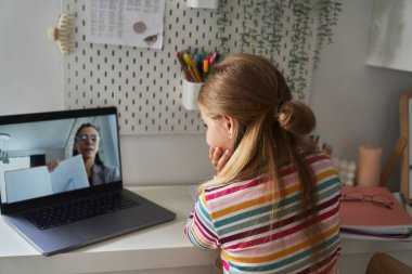 Kafkasyalı ilkokul kızı dizüstü bilgisayarda sohbet ederken yatakta oturuyor.
