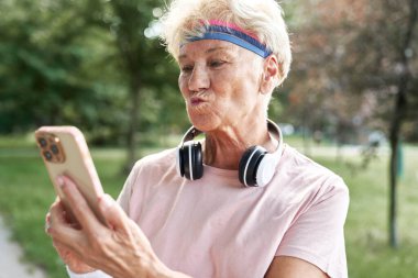 Parkta cep telefonu kullanan yaşlı bir kadın.