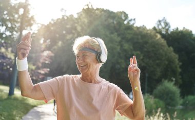 Parkta cep telefonu kullanan yaşlı bir kadın.