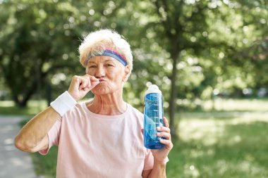 Parkta elinde bir şişe suyla ayakta duran aktif kıdemli kadın.