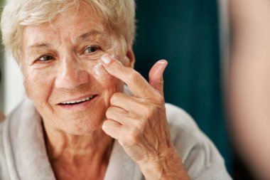 Kıdemli kadın yüz kremi sürüyor.