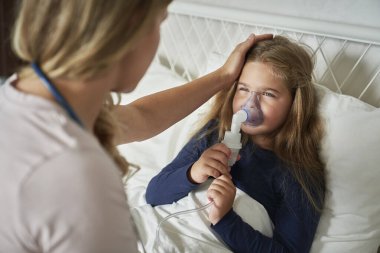 Pediyatrist nebulizör veriyor ve evde hasta bir çocuğa bakıyor.