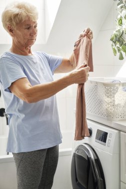 Yaşlı kadın çamaşır makinesini doldurmak üzere.
