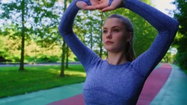 Genç beyaz kadın parkta koşmadan önce geriniyor. 8K 'da kırmızı helyum kamerayla çekildi..  