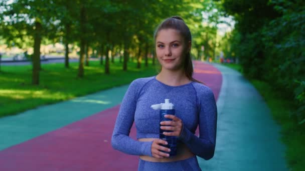 公園でジョギングする前に水でいっぱいのボトルを持っている若い白人女性の肖像画 8KでRedヘリウムカメラで撮影する — ストック動画