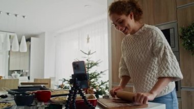 Beyaz kadın zencefilli kurabiye hazırlıyor ve cep telefonundan video görüşmesi yapıyor. 8K 'da kırmızı helyum kamerayla çekildi.. 