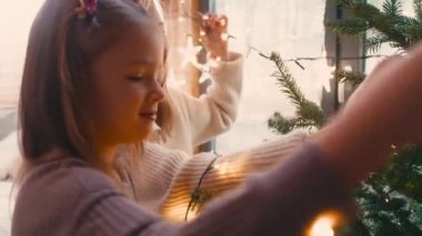 Neşeli anne ve kız Noel ağacını ışıklarla süslüyorlar. 8K 'da kırmızı helyum kamerayla çekildi..   