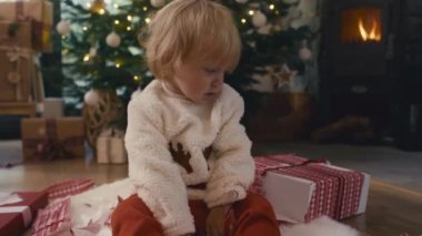 Beyaz, şirin bir bebek Noel hediyesini boşaltıyor. 8K 'da kırmızı helyum kamerayla çekildi..  