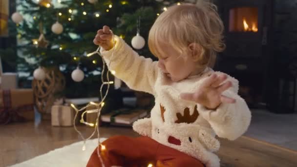 Bebek Yerde Oturuyor Noel Işıklarıyla Oynuyor Kırmızı Helyum Kamerayla Çekildi — Stok video