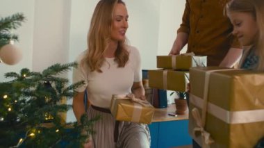 Üç kişilik beyaz bir aile Noel hediyelerini Noel ağacının altına koyuyor. 8K 'da kırmızı helyum kamerayla çekildi..