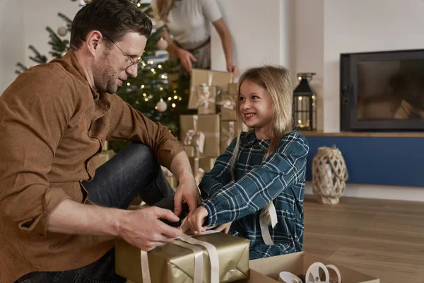 Father and daughter packing Christmas presents next to Christmas tree