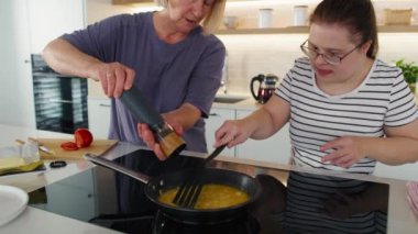 Down sendromlu kadın kahvaltı hazırlarken annesine yardım ediyor. 8K 'da kırmızı helyum kamerayla çekildi..     