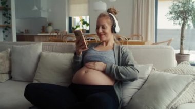 Kafkasyalı hamile kadın kanepede oturup müzik dinliyor.