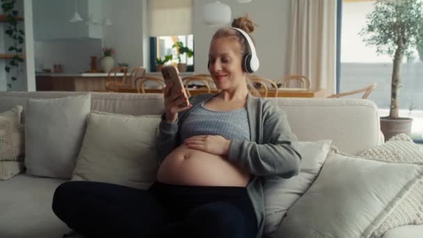 Biała Kobieta Ciąży Siedzi Kanapie Słucha Muzyki — Wideo stockowe